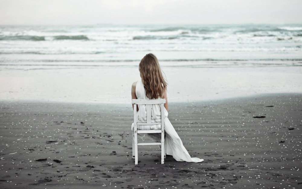 девушка в белом платье сидит на стуле у моря 1000x625